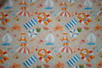 Patterned fabric with cartoon characters, boats, and beach items on a beige background