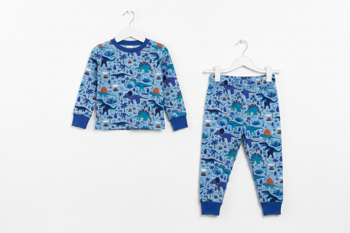 A children's two-piece pajama set consisting of a long-sleeve top and matching pants, both featuring a blue dinosaur pattern, hanging on white hangers against a plain white background. Snazzy Sproglets