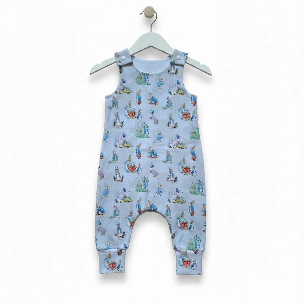 A baby romper in light blue fabric featuring an all-over print of Peter Rabbit characters, snazzy sproglets