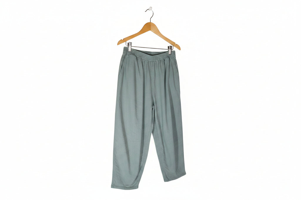 A pair of loose-fitting, light sage green pants with an elastic waistband, laid flat against a solid white background.