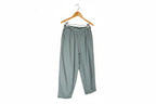 A pair of loose-fitting, light sage green pants with an elastic waistband, laid flat against a solid white background.