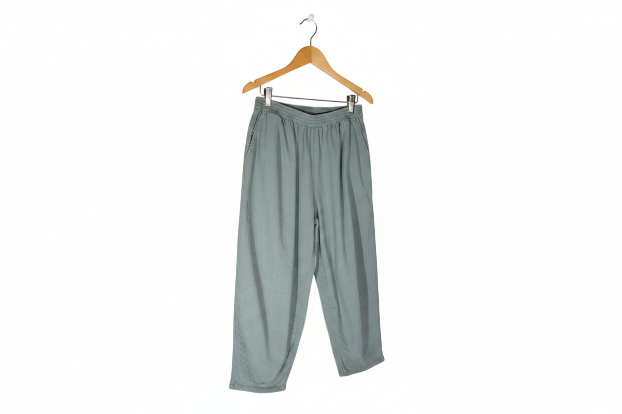 A pair of loose-fitting, light sage green pants with an elastic waistband, laid flat against a solid white background.
