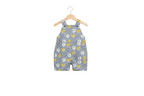 A baby romper in a light blue denim-like fabric with a playful print of cartoon faces in yellow, white, and gray, hanging on a wooden hanger against a plain white background. Snazzy Sproglets