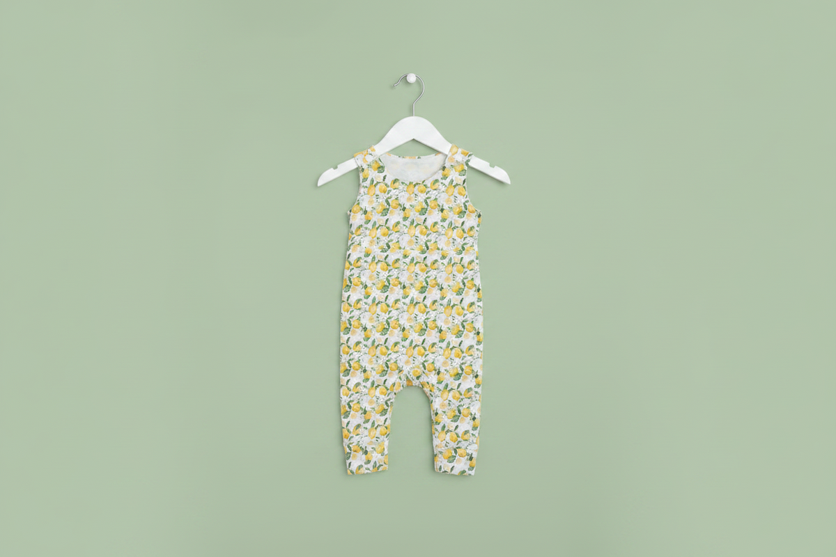 A baby romper with a yellow and white lemon pattern, hanging on a white plastic hanger against a plain white background. Snazzy Sproglets