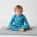 Child wearing a blue outfit with dinosaur and floral patterns on a light gray surface.