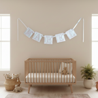 A light blue and white patterned 'MABEL' fabric banner hangs on a beige nursery wall above a wooden crib, snazzy sproglets