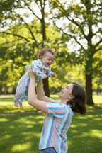 Woman holding a baby in a park with green trees and grass. Snazzy Sproglets