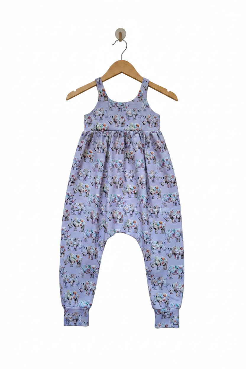 A baby romper in light lavender with an all-over colorful cartoon animal print, featuring a gathered waist and elastic ankle cuffs.