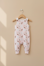 A baby romper in light pink with a scattered pattern of small brown crosses, white flowers, and tiny blue dots, hanging on a wooden hanger against a warm beige background. Snazzy Sproglets
