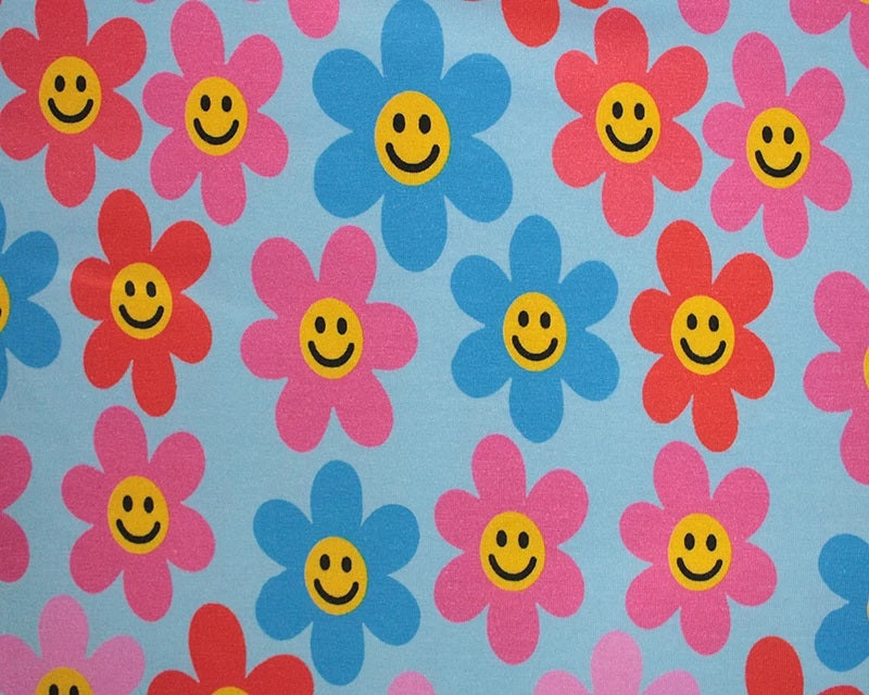 A close-up of a fabric pattern featuring retro smiley-face flowers in pink, blue, and red on a light blue background.
