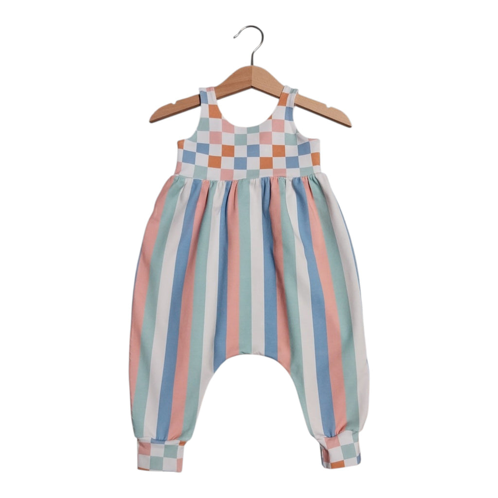 A baby romper with a pastel checkered bodice and vertical pastel stripes, hanging on a wooden hanger against a white background.