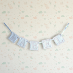 A fabric letter banner spelling 'MABEL' in light blue and white striped quilted letters, hung on a cream patterned wall.