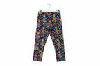 A pair of children's leggings with a colorful print of orange tabby cats, pink and blue flowers, and gold dots on a dark navy background, laid flat on a rustic wooden surface.