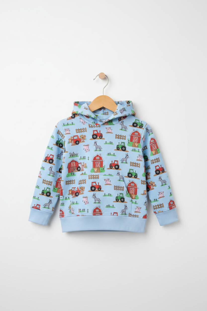A light blue children's hooded sweatshirt with a colorful farm-themed print featuring tractors, barns, and hayrides, hanging on a wooden hanger against a light gray background. Snazzy Sproglets