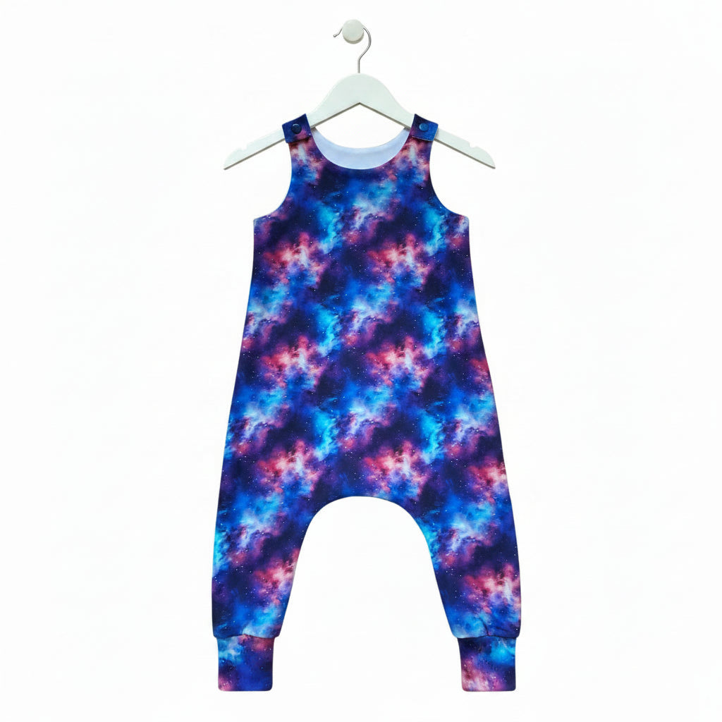A sleeveless baby or toddler one-piece jumpsuit with a vibrant galaxy nebula print in shades of blue, purple, and pink, shown flat against a white background.