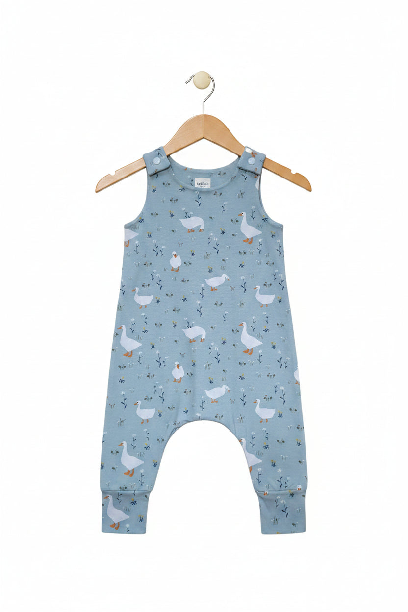 A light green sleeveless baby jumpsuit with an all-over print of white ducks, yellow beaks, and tiny blue and yellow floral details. The jumpsuit features adjustable shoulder straps and a footless cuffed leg design, shown flat against a solid white background.