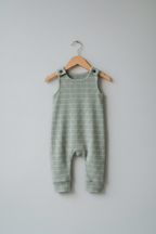 A sleeveless baby romper in sage green with a white windowpane grid pattern, hanging on a wooden hanger against a solid light gray background. Snazzy Sproglets