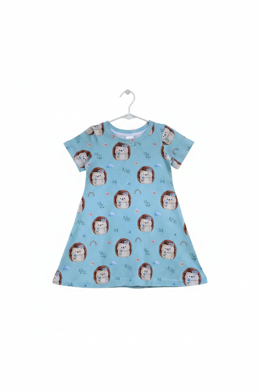 A light green short-sleeve baby dress with an all-over print of cute cartoon hedgehogs, flowers, rainbows, and small plants, shown flat against a white background.