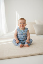 A sleeveless baby romper with a light blue background and an all-over repeating circular medallion pattern in beige, brown, and green, shown flat against a white background.