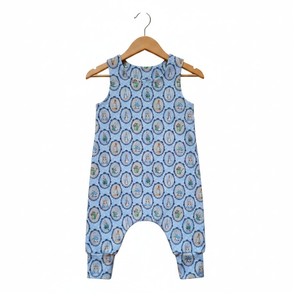 A sleeveless baby romper with a light blue background and an all-over repeating circular medallion pattern in beige, brown, and green, shown flat against a white background.