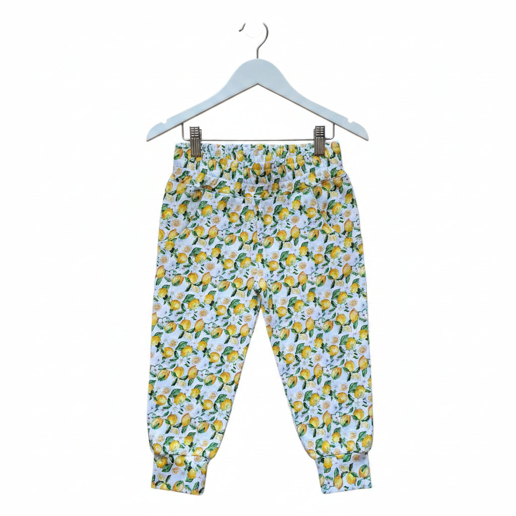 A pair of children's jogger pants featuring an all-over lemon and green leaf pattern on a white background, shown flat against a white backdrop.