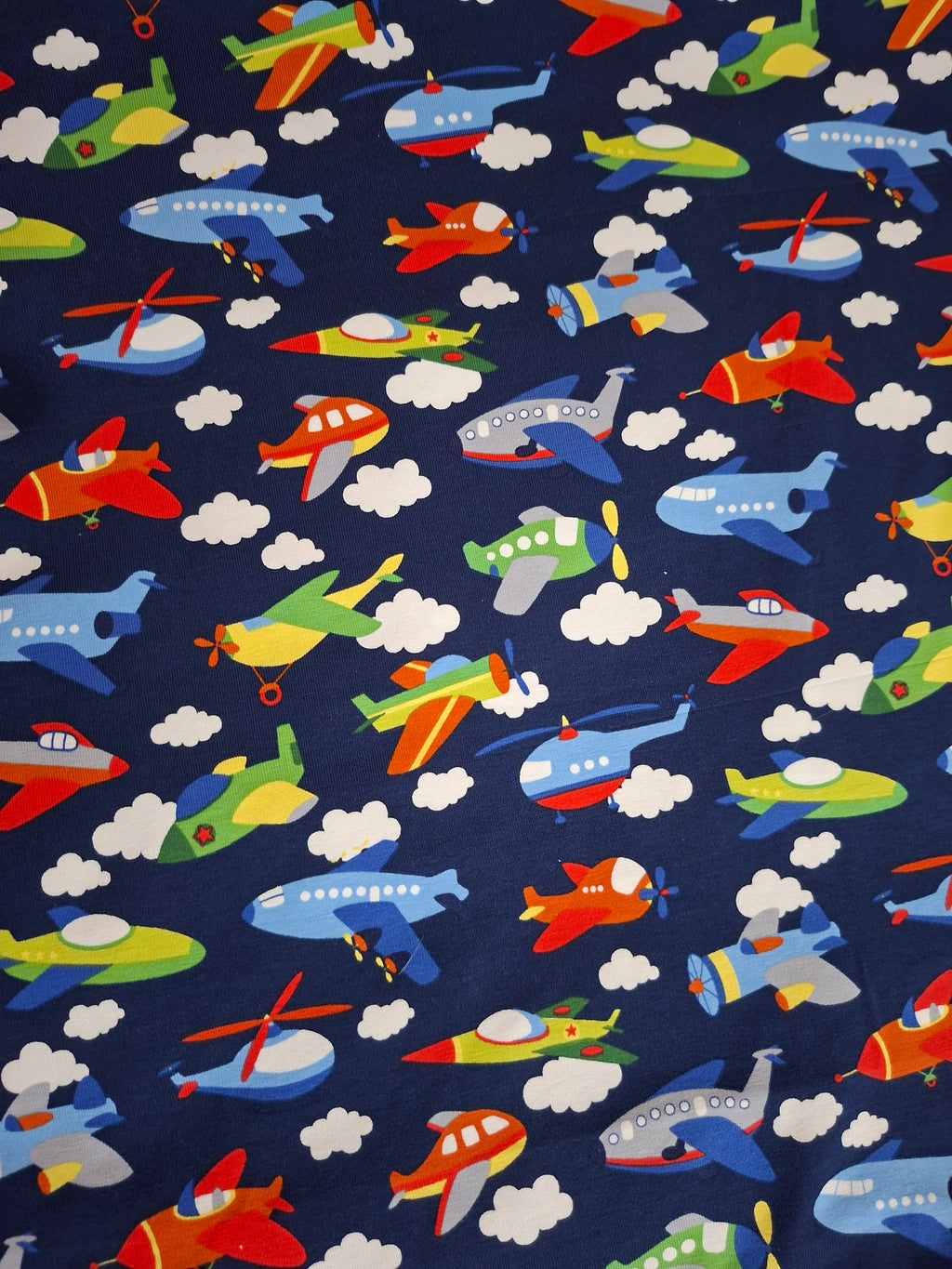 Fabric with colorful airplanes, helicopters, and clouds on a blue background