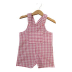 A pink and white gingham baby romper with shoulder straps and a front pocket, hanging on a wooden hanger against a plain white background.