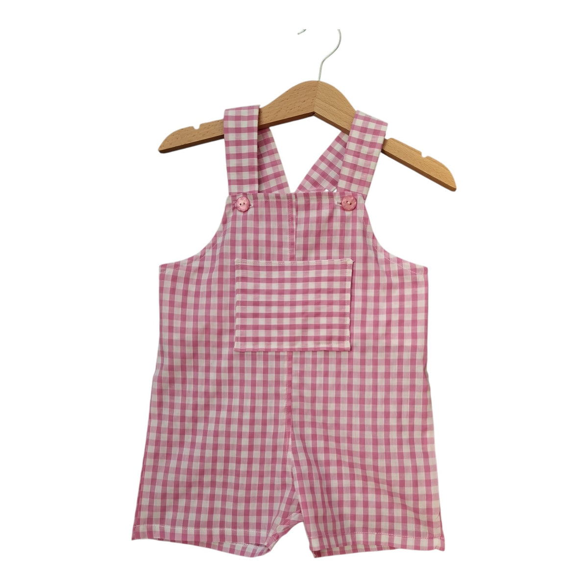 A pink and white gingham baby romper with shoulder straps and a front pocket, hanging on a wooden hanger against a plain white background.