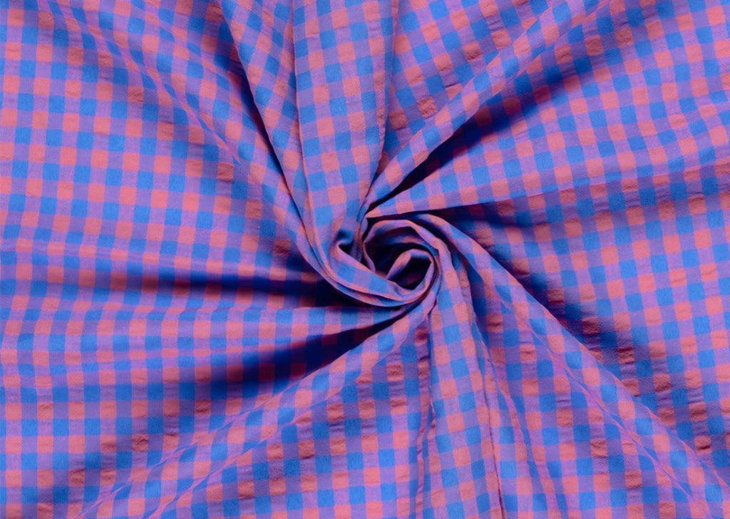 A close-up of a blue and pink gingham fabric arranged in a spiral drape, showing the texture and pattern of the material. Snazzy Sproglets