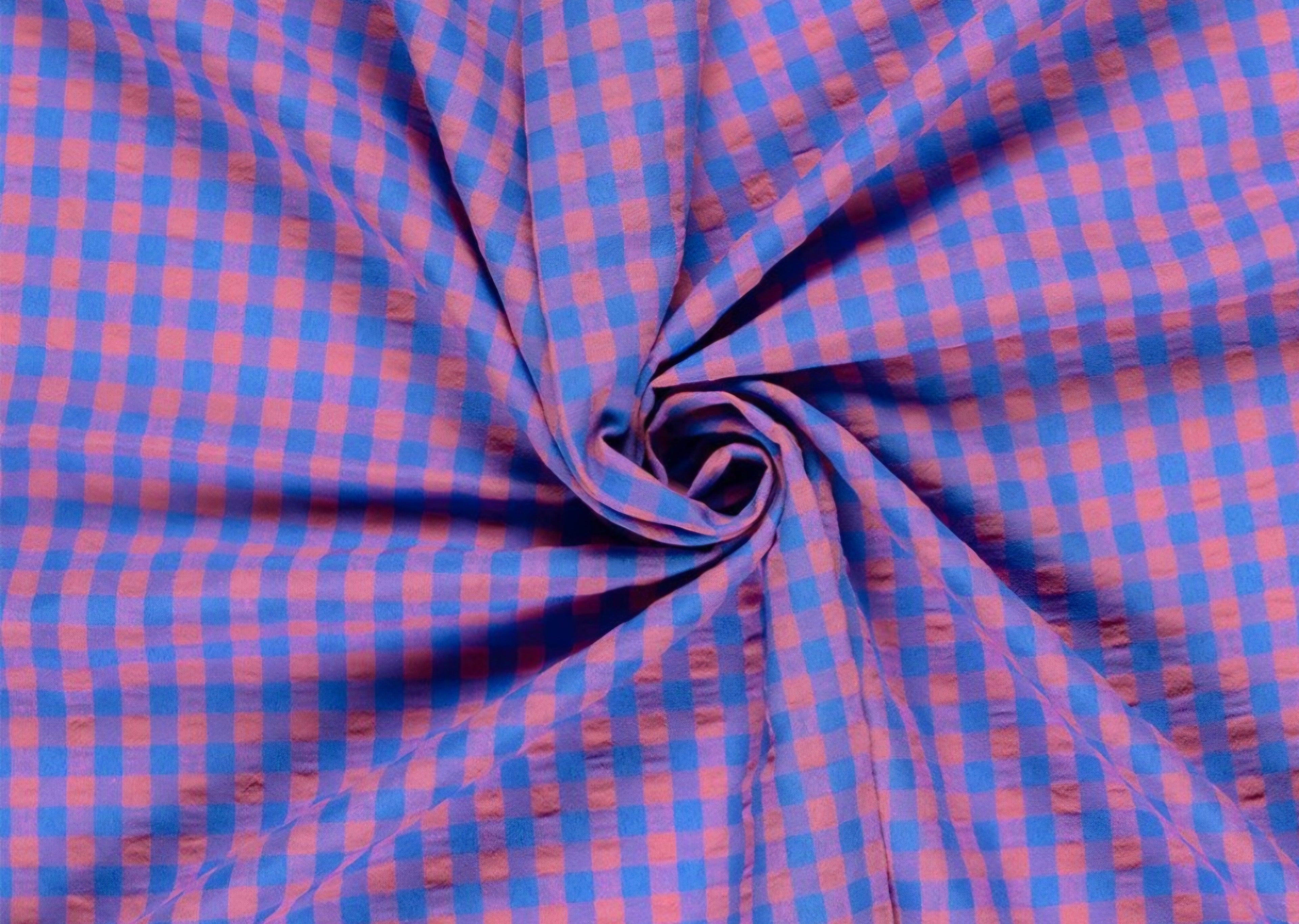 A close-up of a blue and pink gingham fabric arranged in a spiral drape, showing the texture and pattern of the material. Snazzy Sproglets