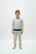 A young boy stands barefoot against a plain white studio background wearing a matching two-piece pajama set. The long-sleeve top and pants are cream-colored with thin multicolored horizontal stripes and small green butterfly motifs, finished with solid blue and mustard yellow trim at the collar, cuffs, and waistband.