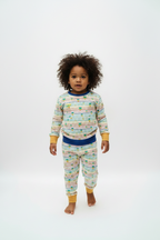 A child modeling a matching two-piece pajama set with a colorful striped pattern and yellow cuffs, on a white studio background.