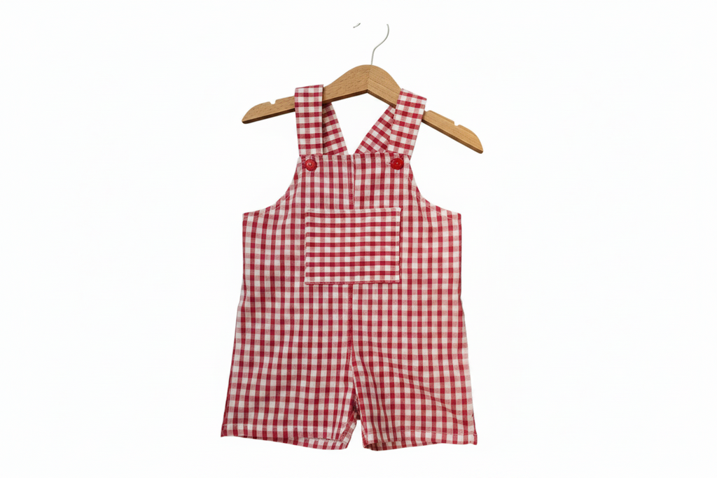 Red and white gingham check baby romper with shoulder straps and a front pocket, hanging on a wooden hanger against a plain white background. Snazzy Sproglets