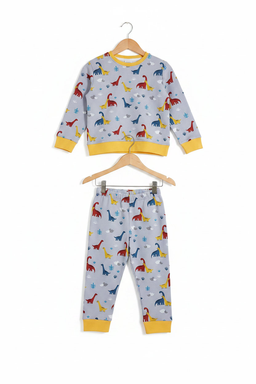 A children's two-piece pajama set consisting of a long-sleeve top and matching pants, hanging on wooden hangers against a plain white background. The pajamas feature a light gray base with a colorful dinosaur print in red, blue, yellow, and green, accented with yellow ribbed cuffs and hem. Snazzy Sproglets