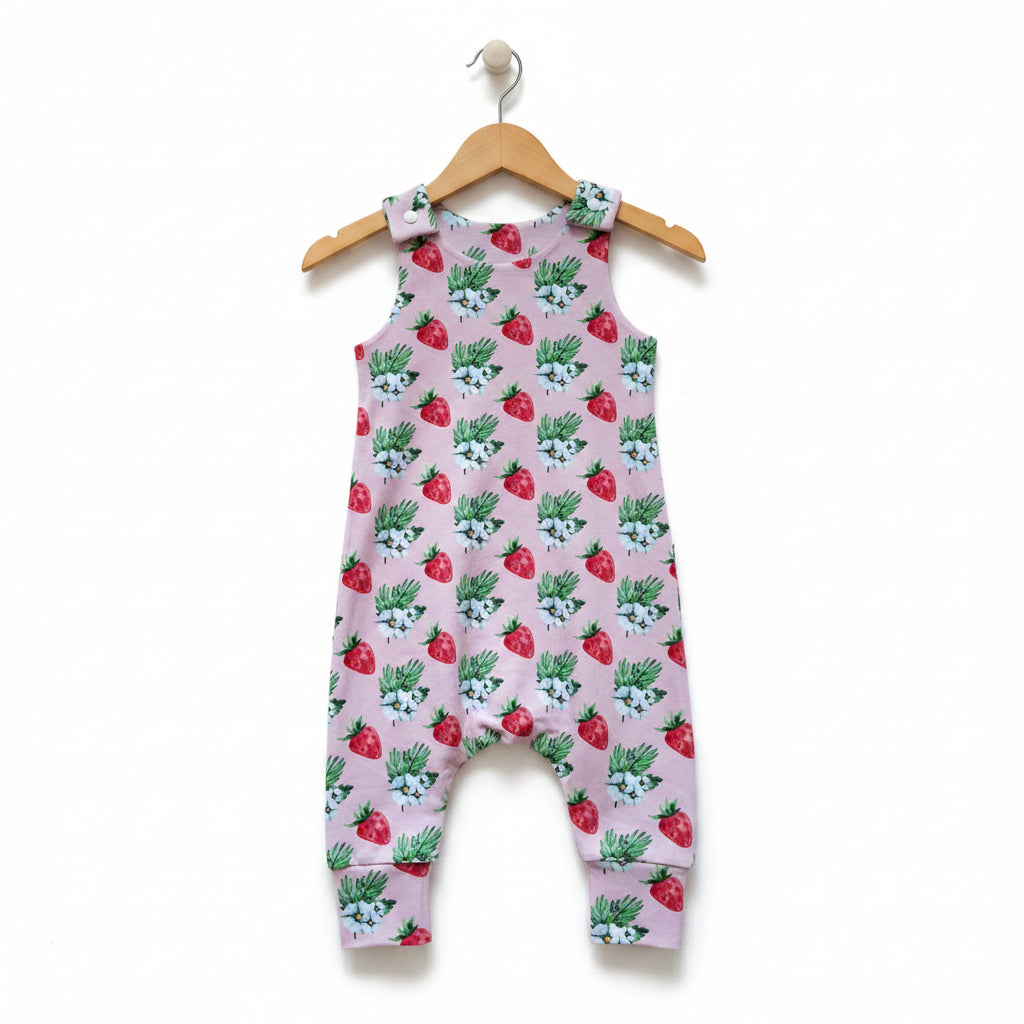 A sleeveless baby romper with an all-over strawberry and blue flower print on a dusty pink background, shown flat against a white background. snazzy sproglets