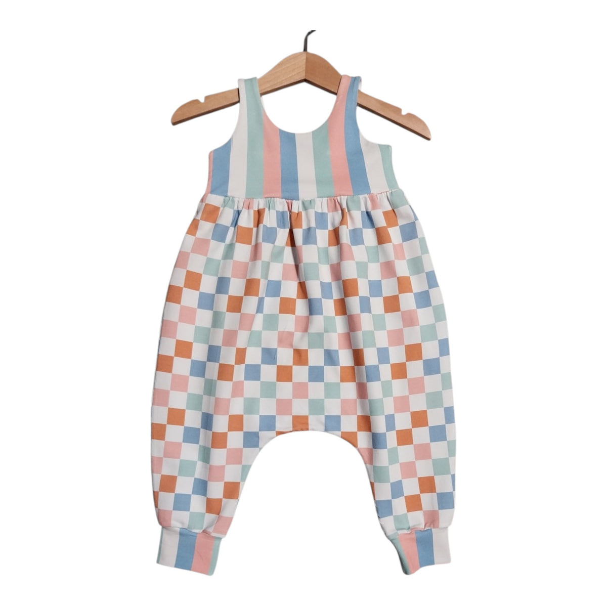 A baby romper with a pastel checkered pattern on the body and striped bodice, hanging on a wooden hanger against a white background.