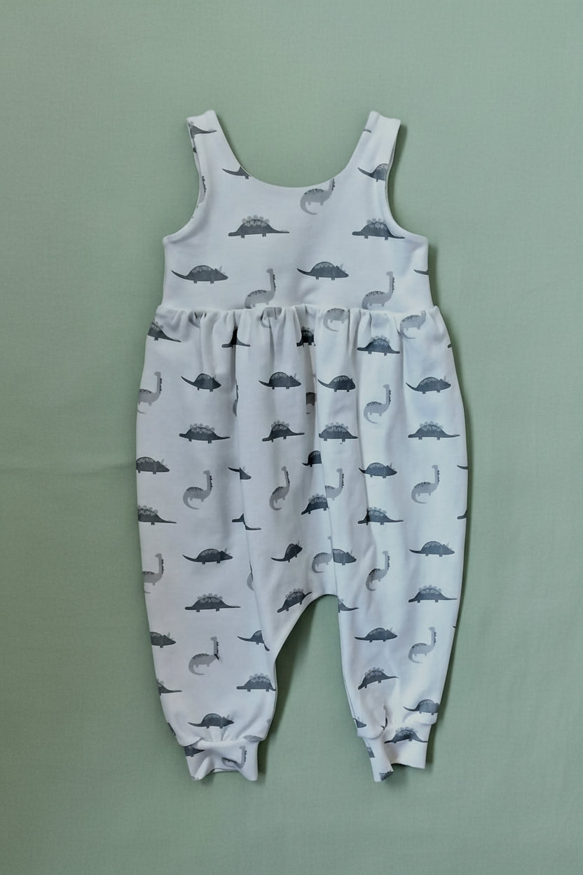 A baby romper in a winter white color, featuring an all-over print of grey dinosaur silhouettes, 