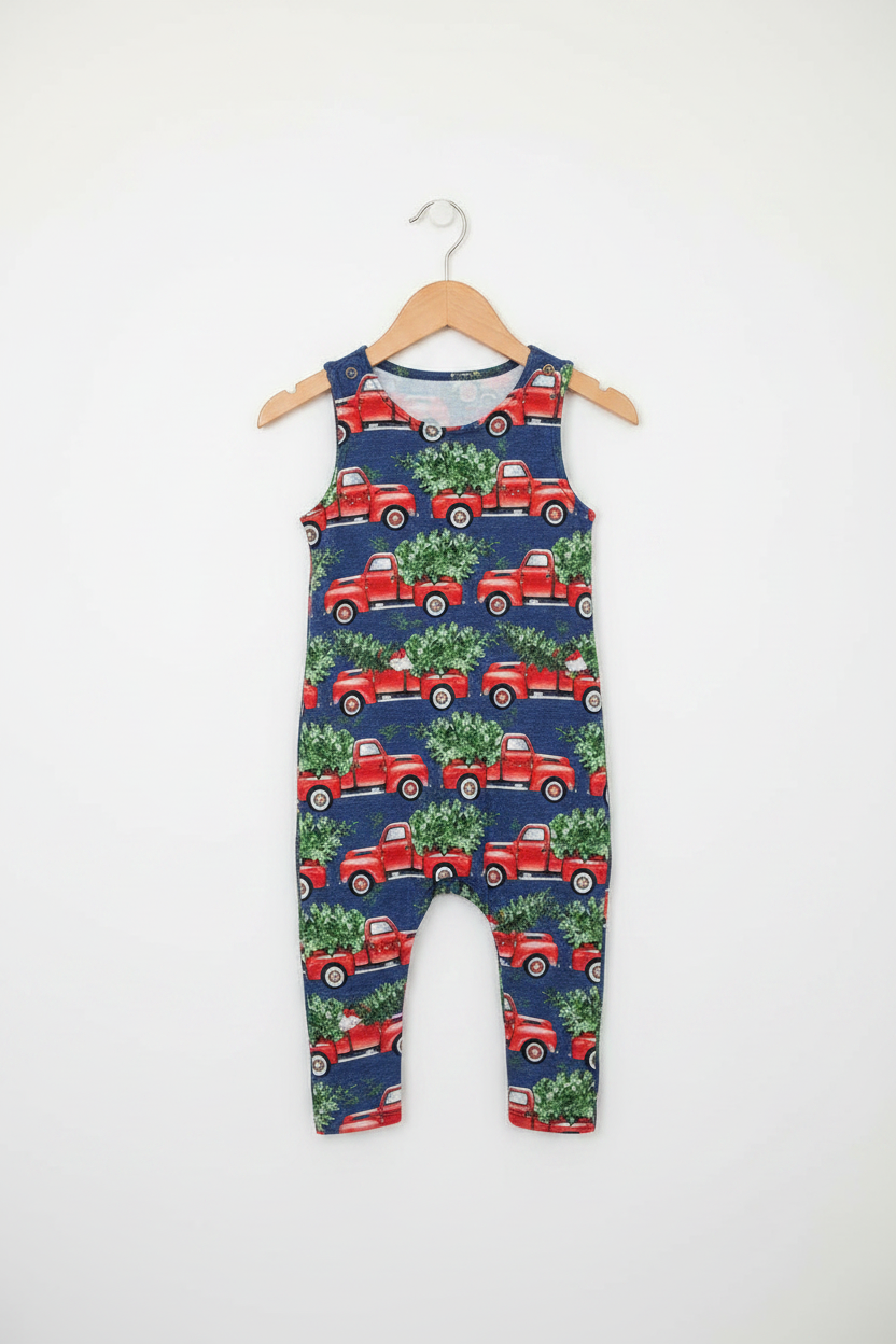 A sleeveless baby romper with an all-over print of red vintage trucks carrying green Christmas trees, hanging on a wooden hanger against a plain white wall. Snazzy Sproglets