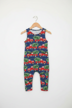 A sleeveless baby romper with an all-over print of red vintage trucks carrying green Christmas trees, hanging on a wooden hanger against a plain white wall. Snazzy Sproglets